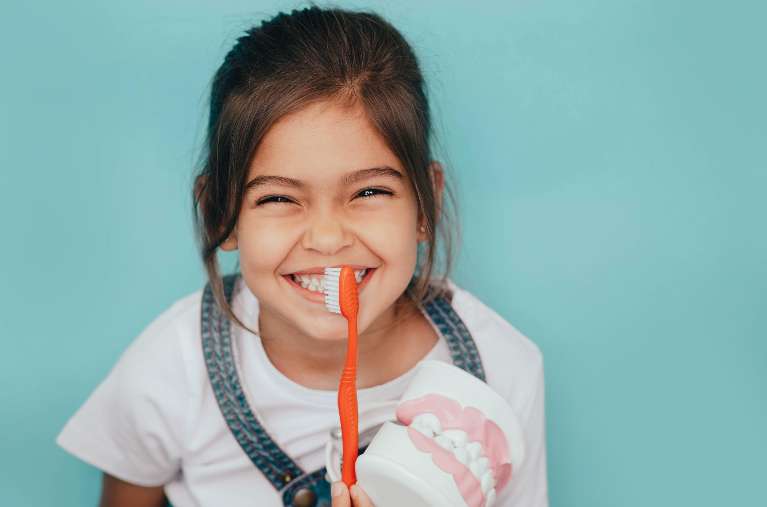 girl holding toothbrush smiling | pediatric dentist dumbo